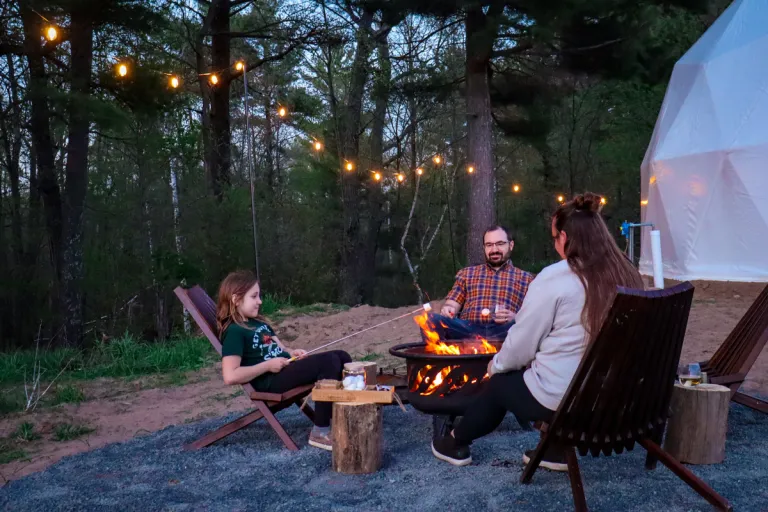 Family roasting s'mores around the campfire outside the dome at night